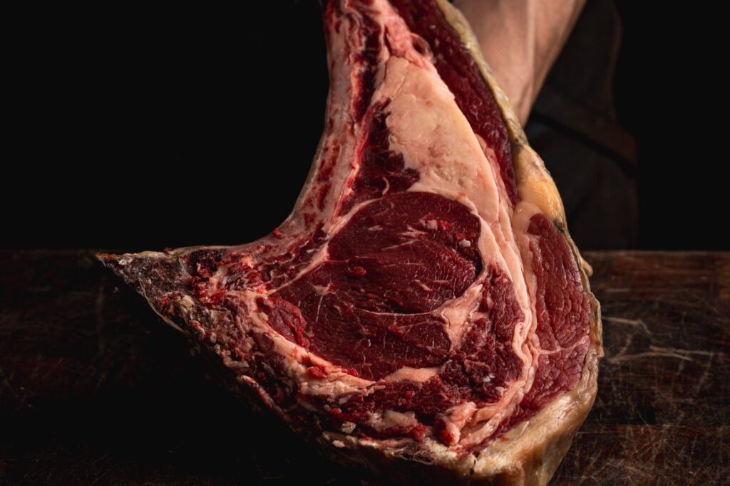 Chuletón de vaca con hueso sostenido sobre una tabla de madera, con el marmoleado y la grasa de cobertura a la vista