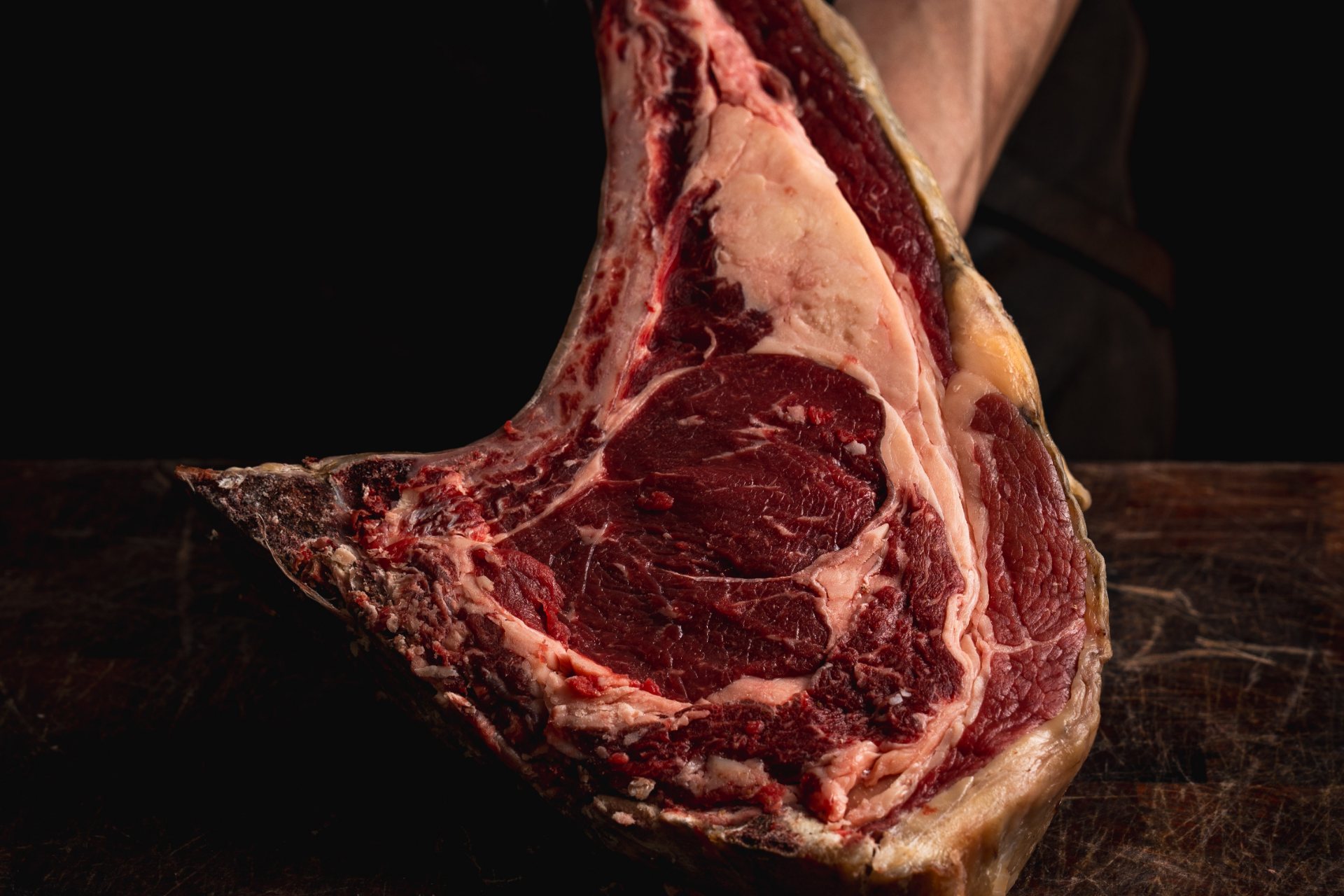 Chuletón de vaca con hueso sostenido sobre una tabla de madera, con el marmoleado y la grasa de cobertura a la vista